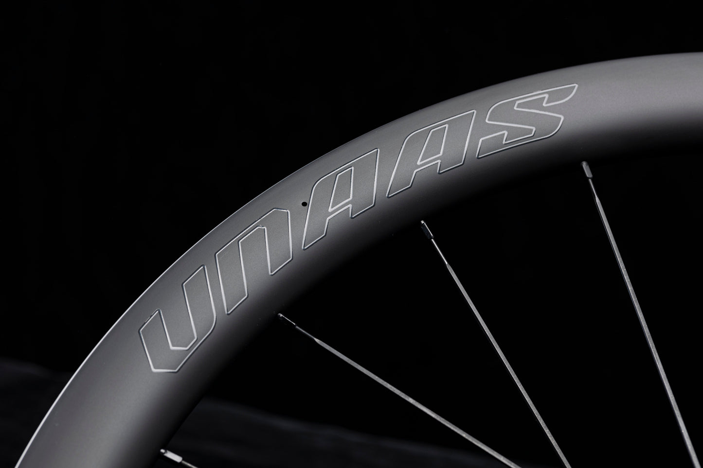 Close up of UNAAS HARD H50D matte black carbon wheelset rim with white UNAAS logo and silver spokes.