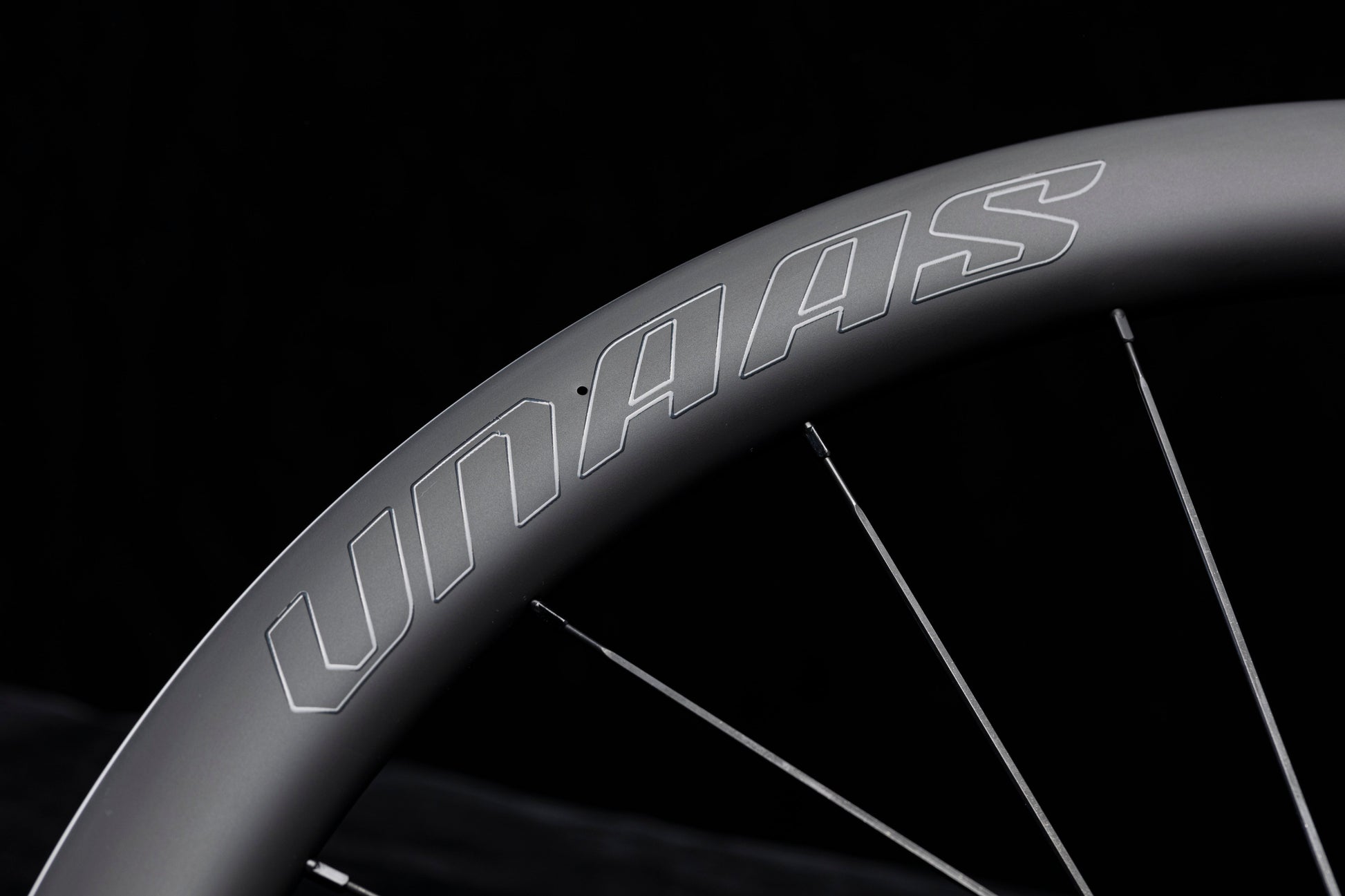 Close up of UNAAS HARD H50D matte black carbon wheelset rim with white UNAAS logo and silver spokes.
